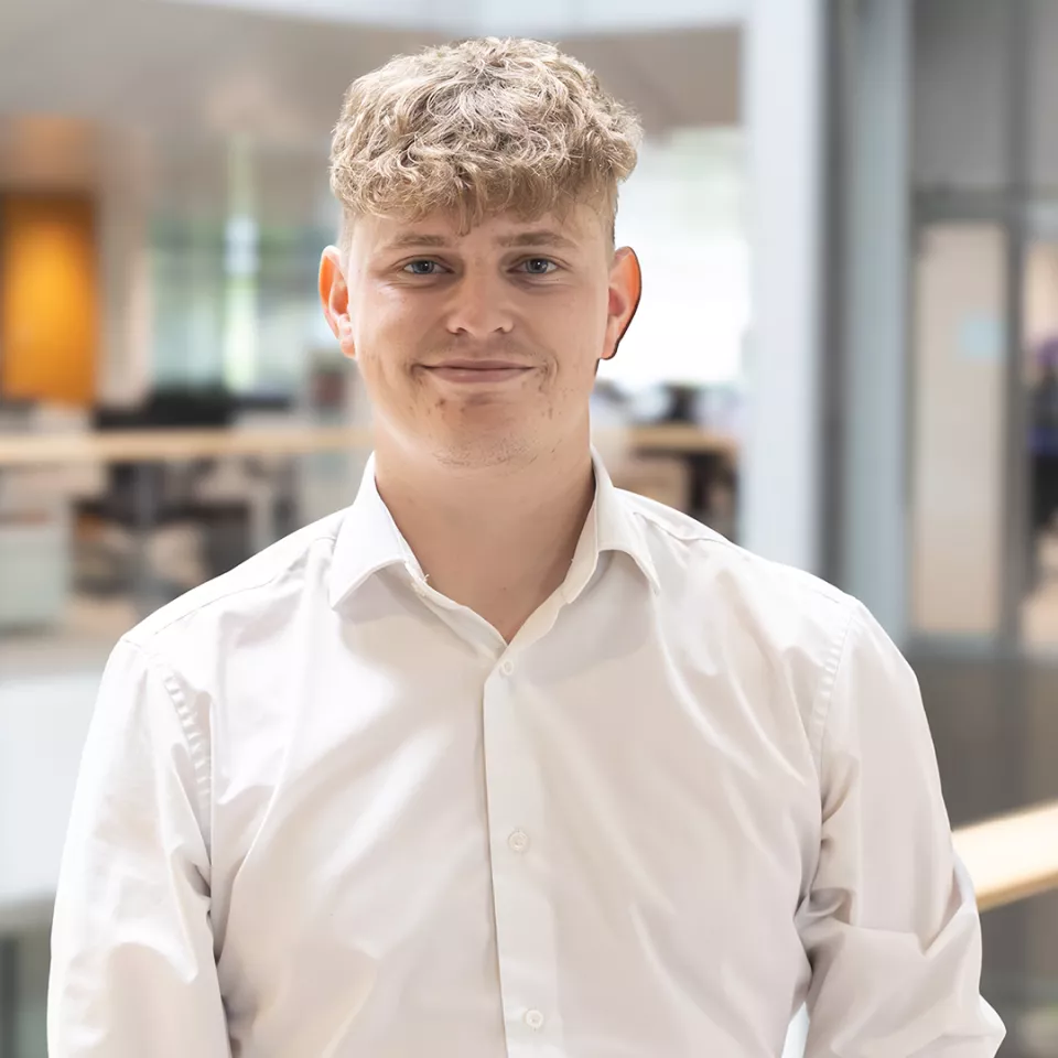 This shows a  smiling, blonde haired male colleague from the UK&I sales team standing on a balcony within the office atrium   