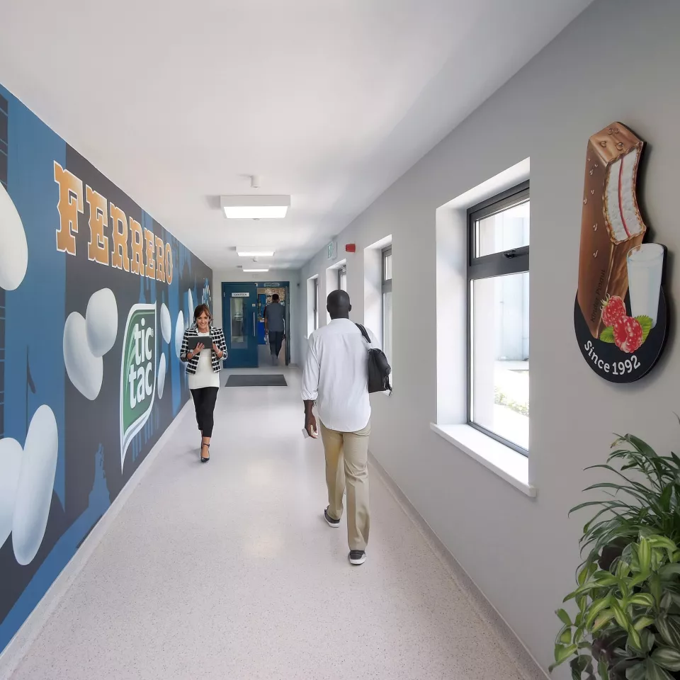 A man in the office corridor which has wall art of Tic Tac on one wall