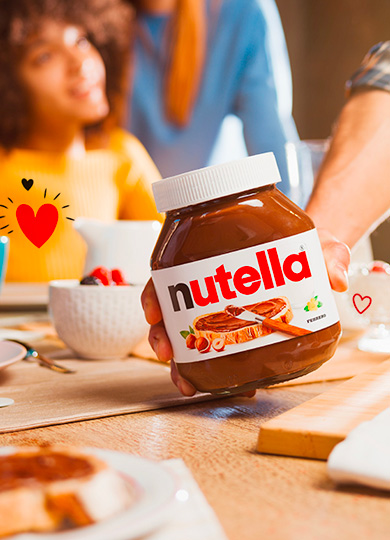 Hand holding a Nutella jar at a breakfast table.