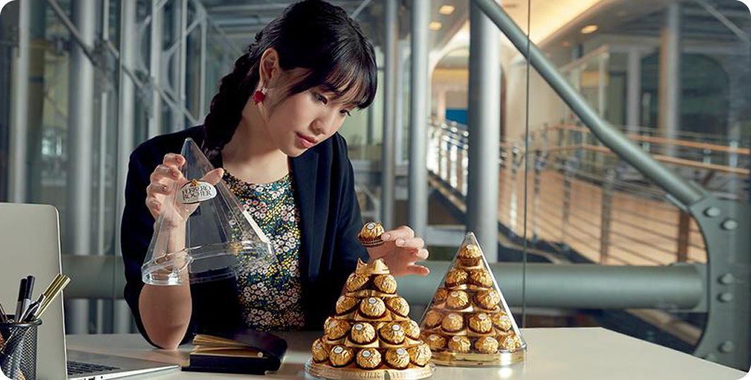 Person arranging chocolate confections into a pyramid on a table.
