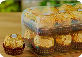 Transparent box of Ferrero Rocher chocolates on a wooden table with one praline outside
