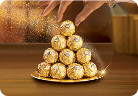 Hand placing Ferrero Rocher on a golden pyramid display on a wooden table.