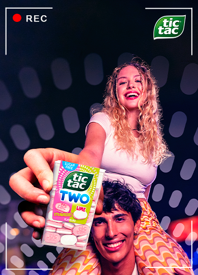 A boy and a girl holding a Tic Tac Two Strawberry Lime pack in a colorful night-time setting