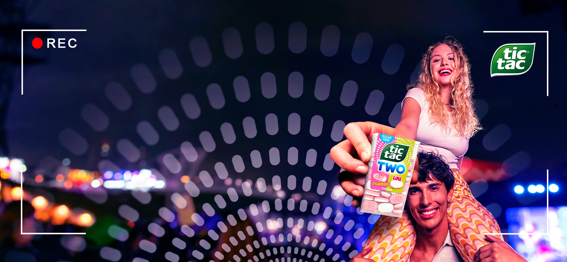 A boy and a girl holding a Tic Tac Two Strawberry Lime pack in a colorful night-time setting