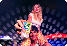 A boy and a girl holding a Tic Tac Two Strawberry Lime pack in a colorful night-time setting