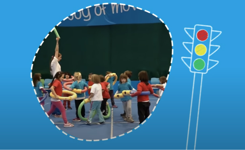 Teacher showing green hoop to group of children in sports hall.