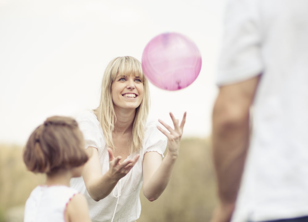 Woman, man and girl playing with pink ball.