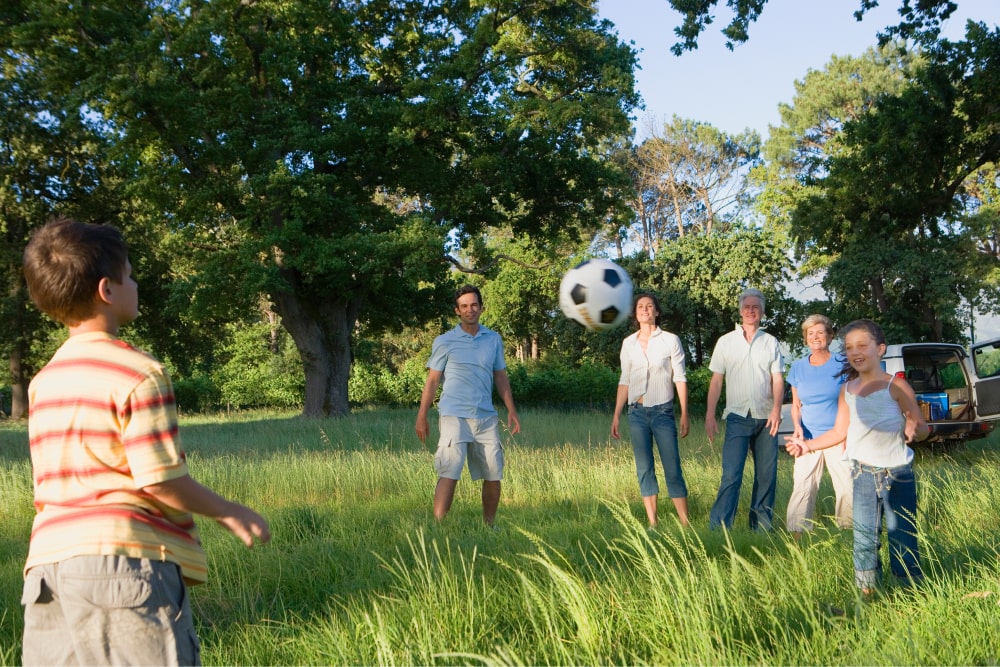 Four adults and two children playing with a football outdoors.