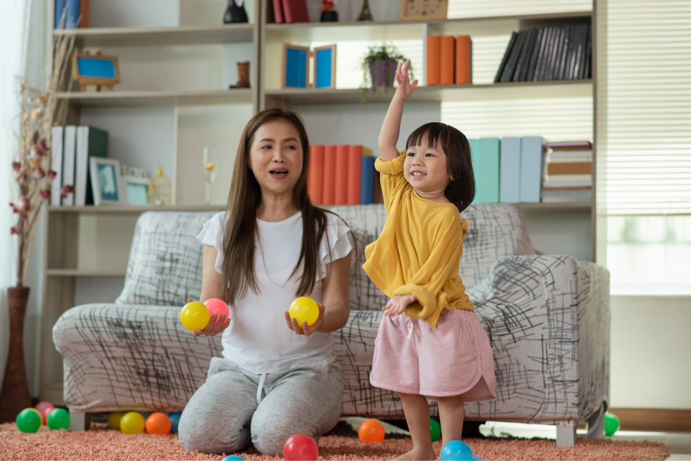 Mother and child daughter playing with colourful balls in sitting room.