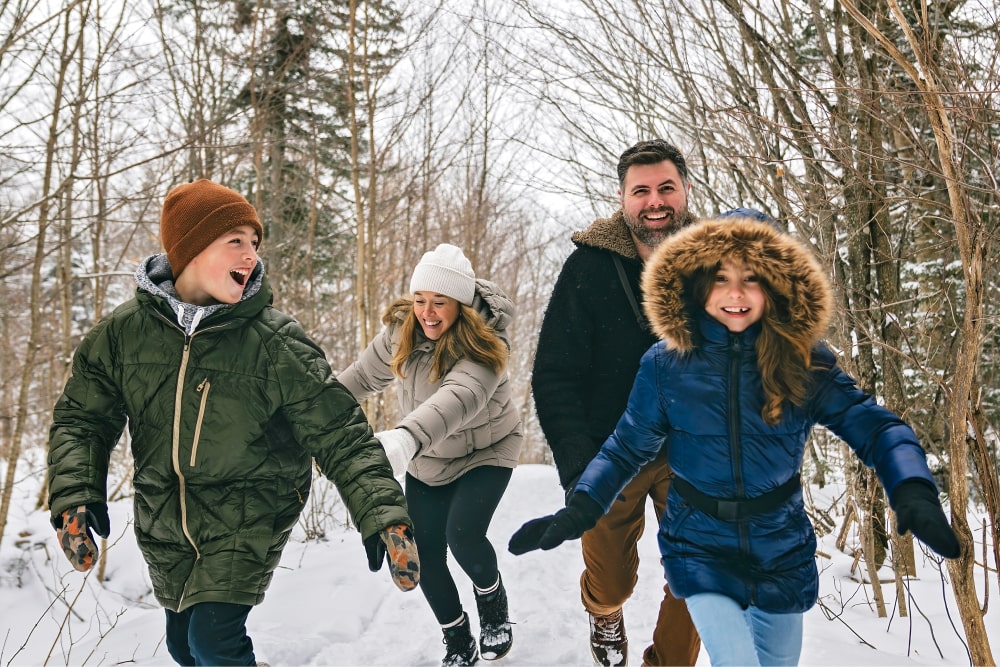 Two adults and two children smiling and walking in a snowscape
