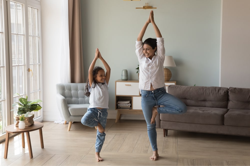 Mother and daughter doing the tree pose in a sitting room.