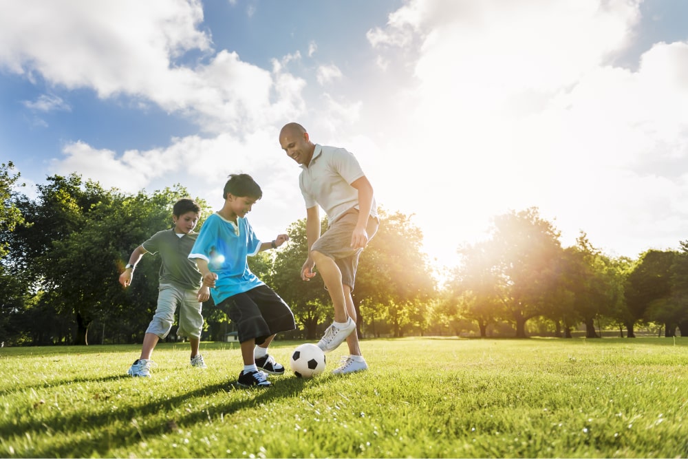 Father playing football with two boys in park.