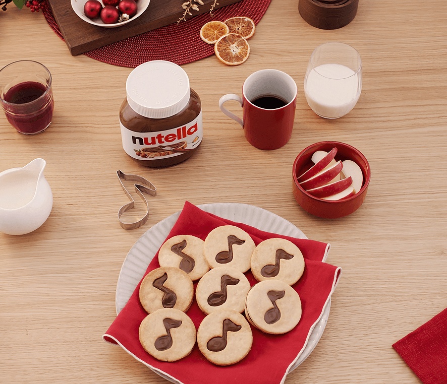 Round Christmas sugar cookies decorated with Nutella musical notes next to a Nutella jar.