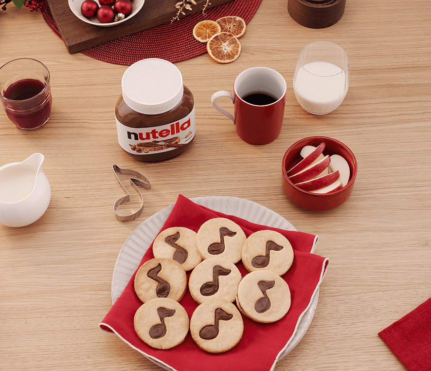 Round Christmas sugar cookies decorated with Nutella musical notes next to a Nutella jar.